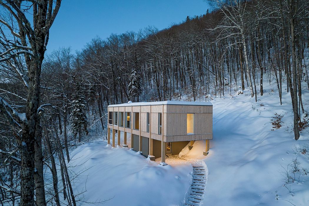 Contemporary cabin with large windows nestled in snowy woods at dusk.