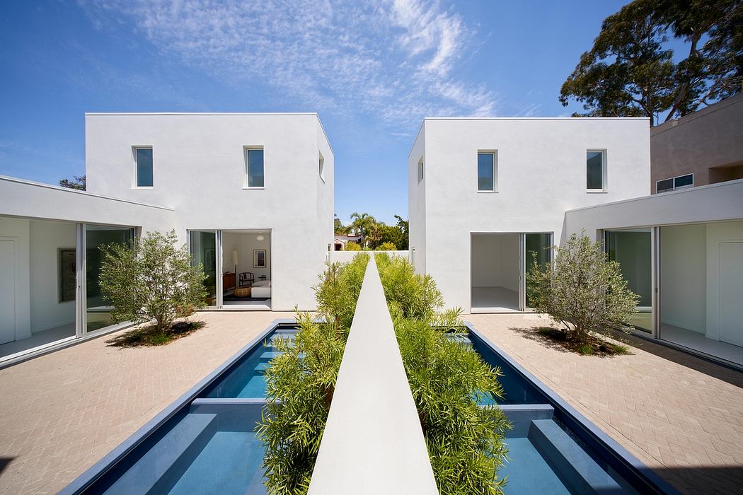 Modern white houses with pools and greenery set against a blue sky.