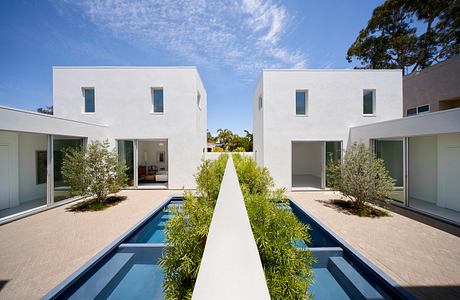 Modern white houses with pools and greenery set against a blue sky.