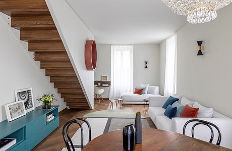 Inviting open-concept living space with modern wooden stairs, vibrant colors, and a chandelier.