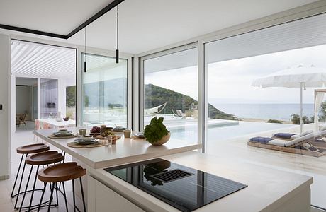 Sleek, minimalist kitchen with floor-to-ceiling glass walls showcasing stunning ocean view.