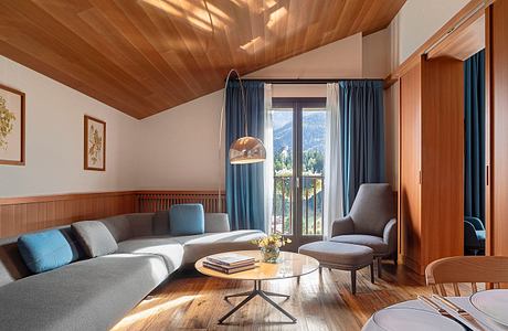 Cozy living room with wooden ceiling, plush furniture, and mountain views through large window.