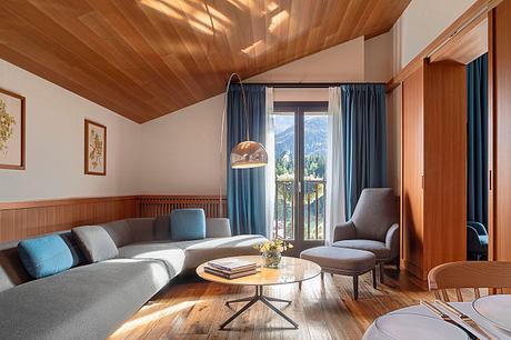 Cozy living room with wooden ceiling, plush furniture, and mountain views through large window.