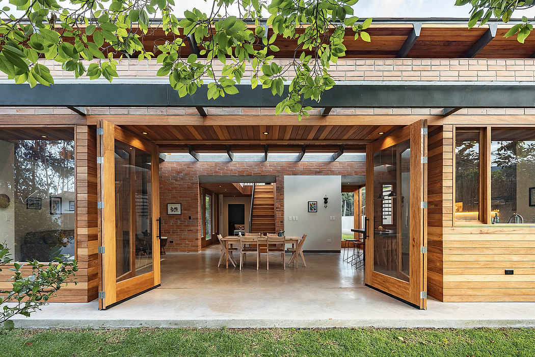 A modern wooden and brick structure with large sliding glass doors, exposed beams, and lush greenery.