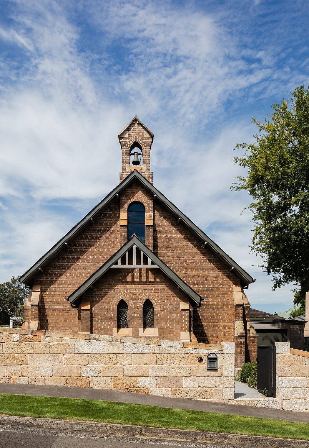 A brick church with a bell tower and arched windows, set against a blue sky and surrounded by trees.