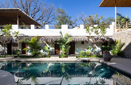 A tropical resort-style backyard with a pool and thatched-roof cabanas.