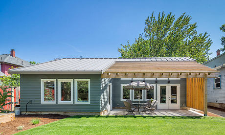 Modern exterior with gray siding, metal roof, patio, and lush landscaping.