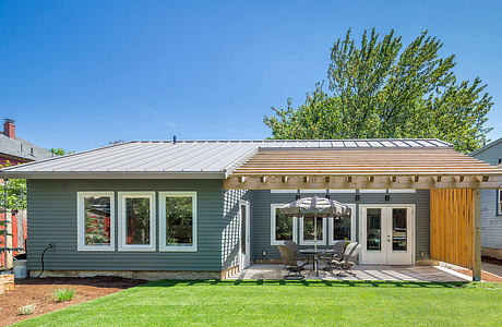 Modern exterior with gray siding, metal roof, patio, and lush landscaping.