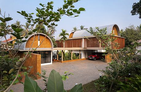 A modern, tropical-inspired building with arched entrances, wooden screens, and lush vegetation.