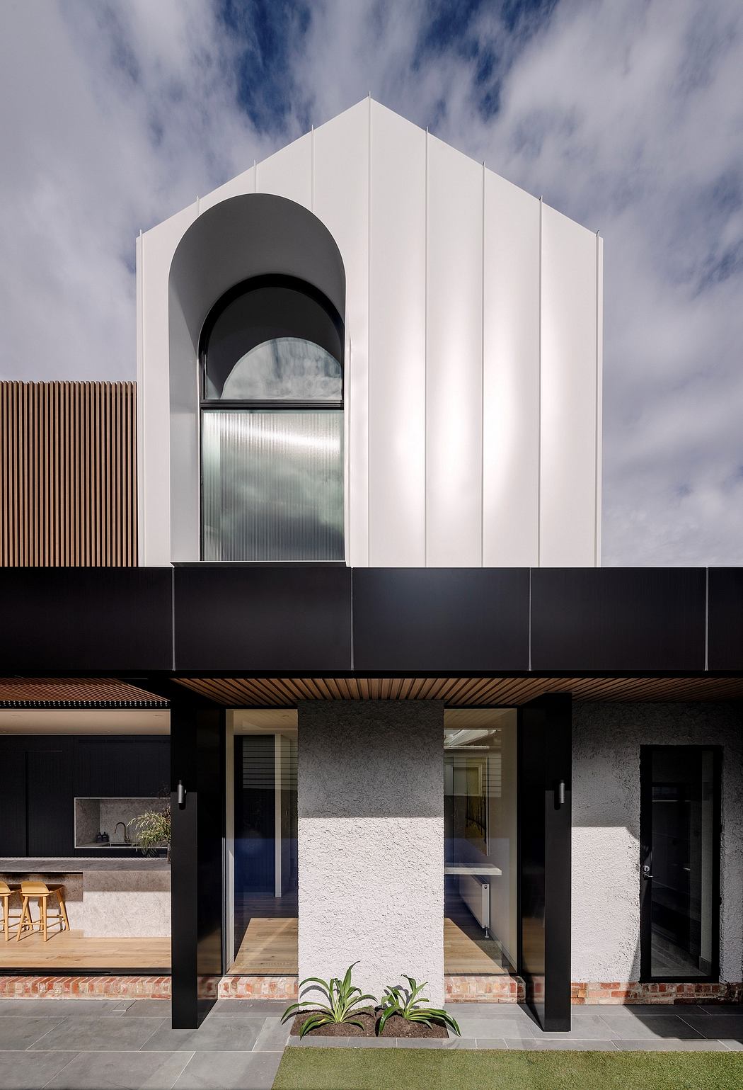 Modern architectural design with contrasting white and black facades, arched entryway, and wood accents.