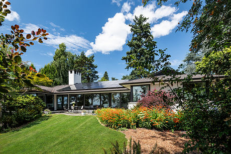 A modern, single-story home with large windows, surrounded by lush, well-manicured landscaping.