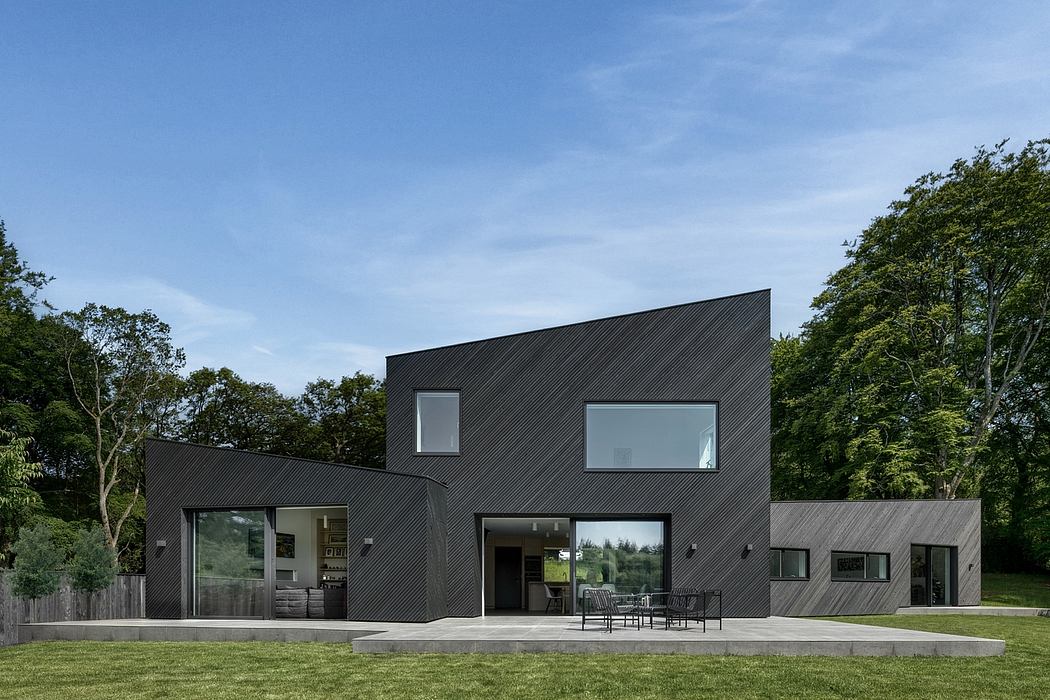 Contemporary two-story house with angular black exterior and large windows overlooking green landscape.