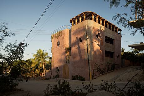 Striking adobe-style structure with intricate wooden beams and balconies amidst lush greenery.