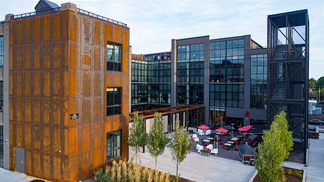 Modern architectural design with a mix of glass, steel, and rust-colored panels, featuring an outdoor seating area.