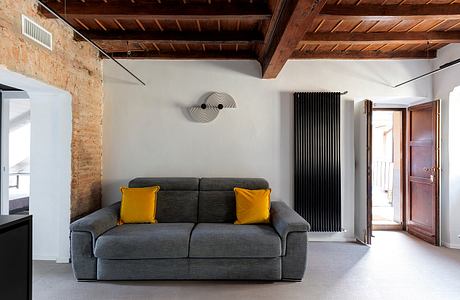 Cozy loft-style living room with exposed brick walls, wooden ceiling, and sleek gray sofa.