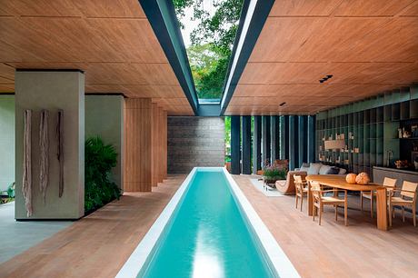 Modern indoor space with a long pool, wooden ceiling, and stylish furniture.