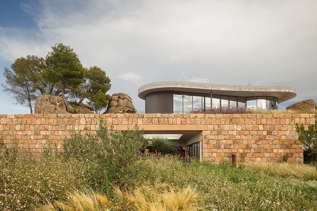 Futuristic house with curved design atop stone walls in natural setting.