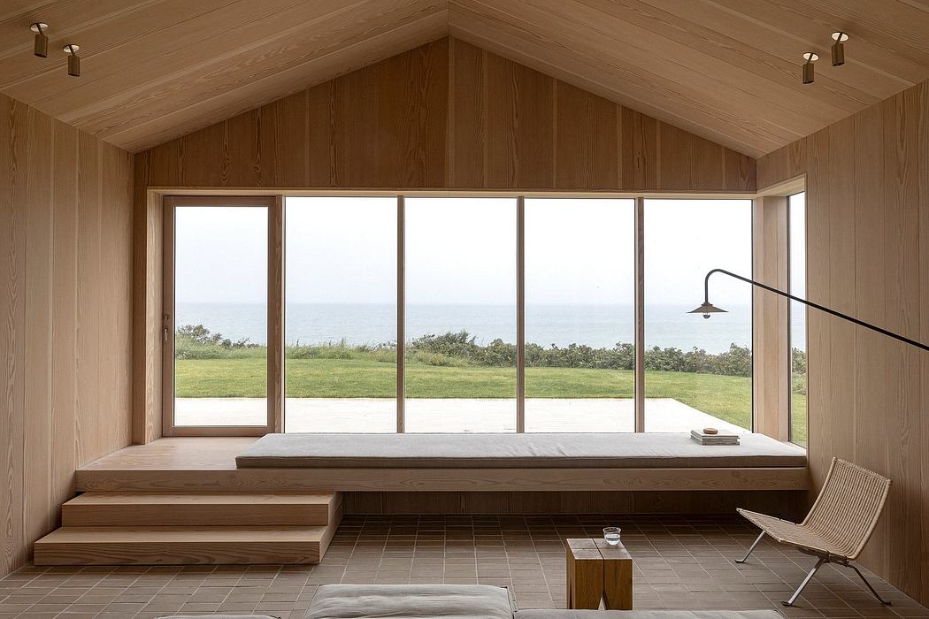 Minimalist wooden interior with large window overlooking the sea.