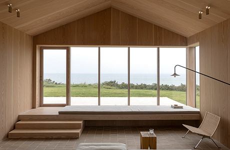 Minimalist wooden interior with large window overlooking the sea.