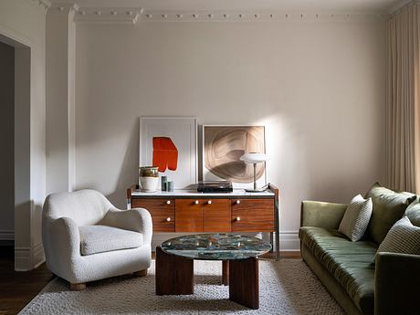 Elegant living room with white armchair, green sofa, and wooden furniture.