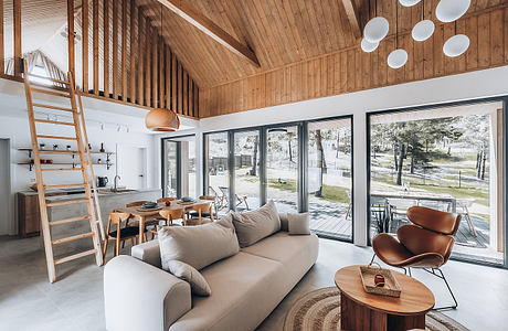 A cozy cabin interior with a vaulted wooden ceiling, large windows, and modern furniture.