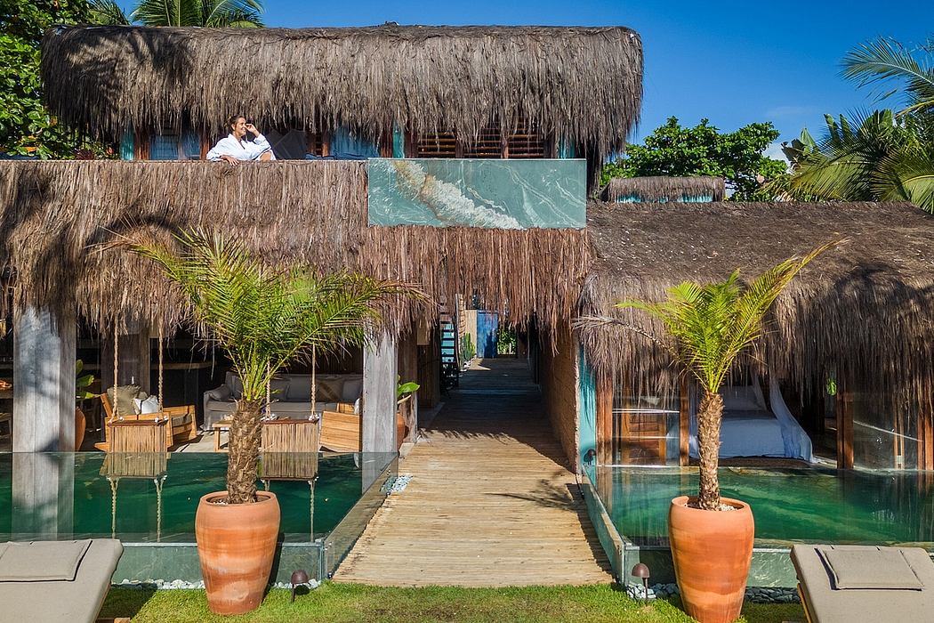 A tropical, open-air resort with thatched-roof structures, palm trees, and a walkway over a pool.