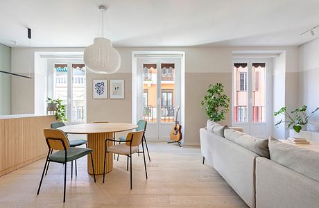 Bright, open-concept living space with wooden dining table, neutral furniture, and large windows.