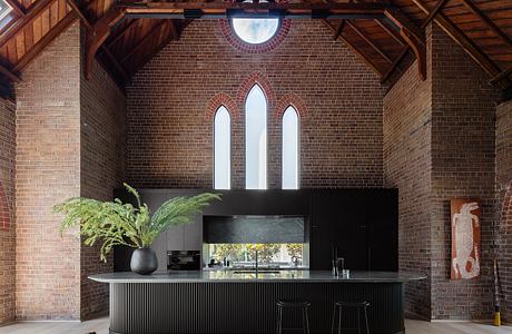 Stunning brick interior with arched windows, modern black kitchen island, and a small dog.