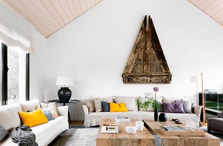 Modern living room with white sofas, yellow accents, and a unique triangular artwork.