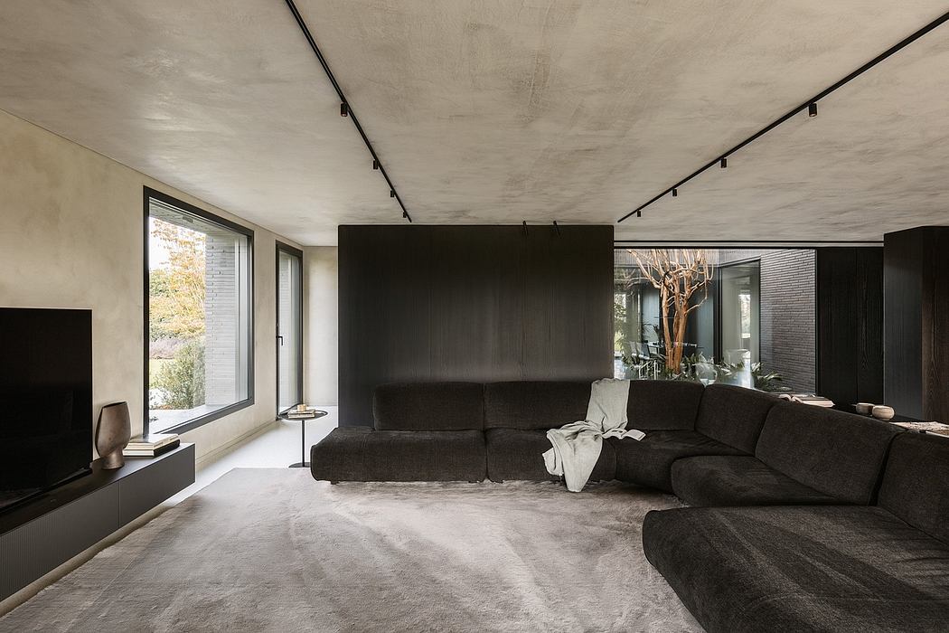Dark, minimalist living room with concrete ceiling, track lighting, and large sectional sofa.