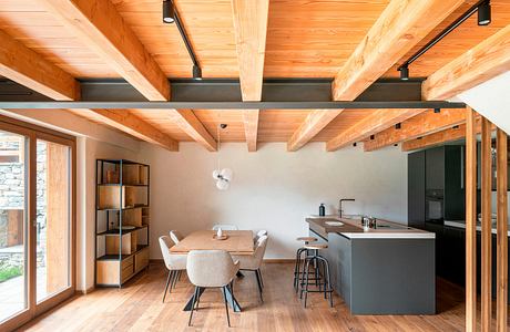 A cozy, modern open-plan living area with wooden beams, gray cabinetry, and a dining table.