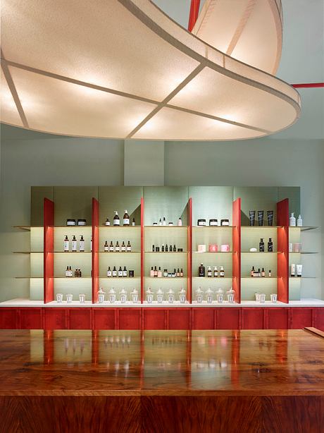 The room features a modern, minimalist design with a large, curved light fixture and sleek, red-accented shelving displaying various products.