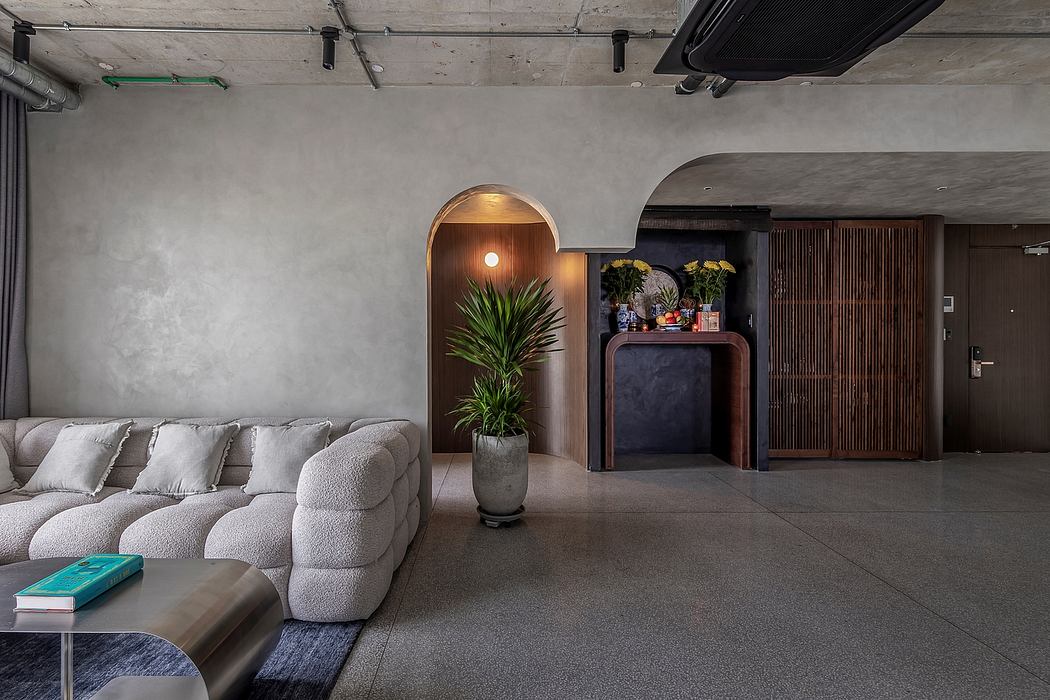 The modern interior features a gray concrete ceiling, plush gray sofa, and a built-in plant display.