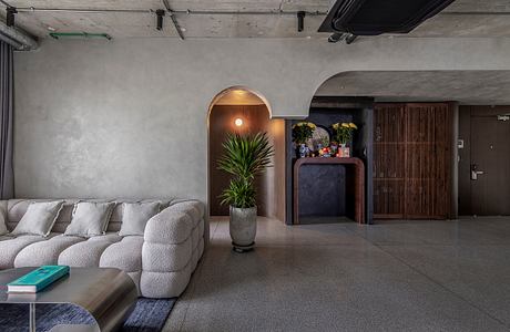 The modern interior features a gray concrete ceiling, plush gray sofa, and a built-in plant display.