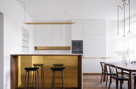 Minimalist kitchen with brass island, herringbone floor, and pendant lights.