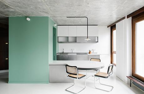 Minimalist kitchen with green accent wall, stainless steel appliances, and wooden chairs.