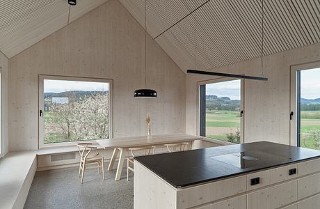 Minimalist interior with exposed wood beams, large windows, and a central kitchen island.