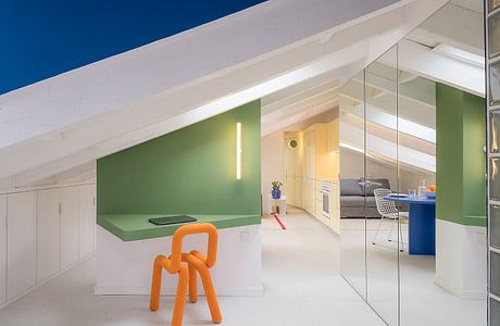 Bright, modern attic space with green accent wall, white floor, and playful orange chair.