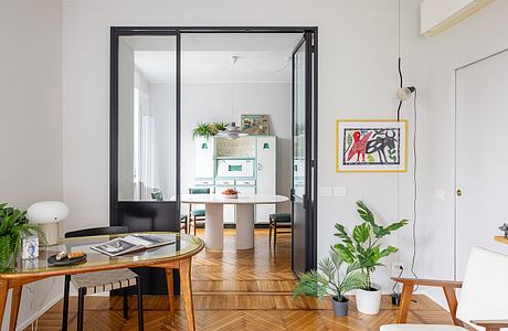 A modern, open-concept living space with sleek black-framed glass doors, wood floors, and colorful art.