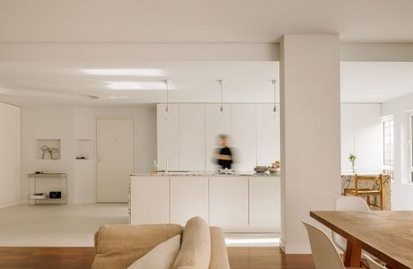 Open-concept living space with minimalist kitchen, wooden dining table, and natural lighting.