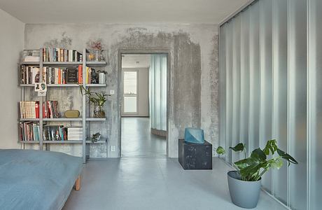 Minimalist living room with industrial-style shelving, potted plants, and concrete walls.