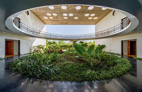 Circular atrium with lush tropical plants and reflective floor in modernist building.