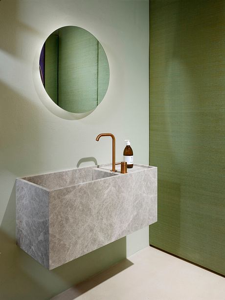 A modern bathroom vanity with a marble sink and a round mirror set against a green wall.