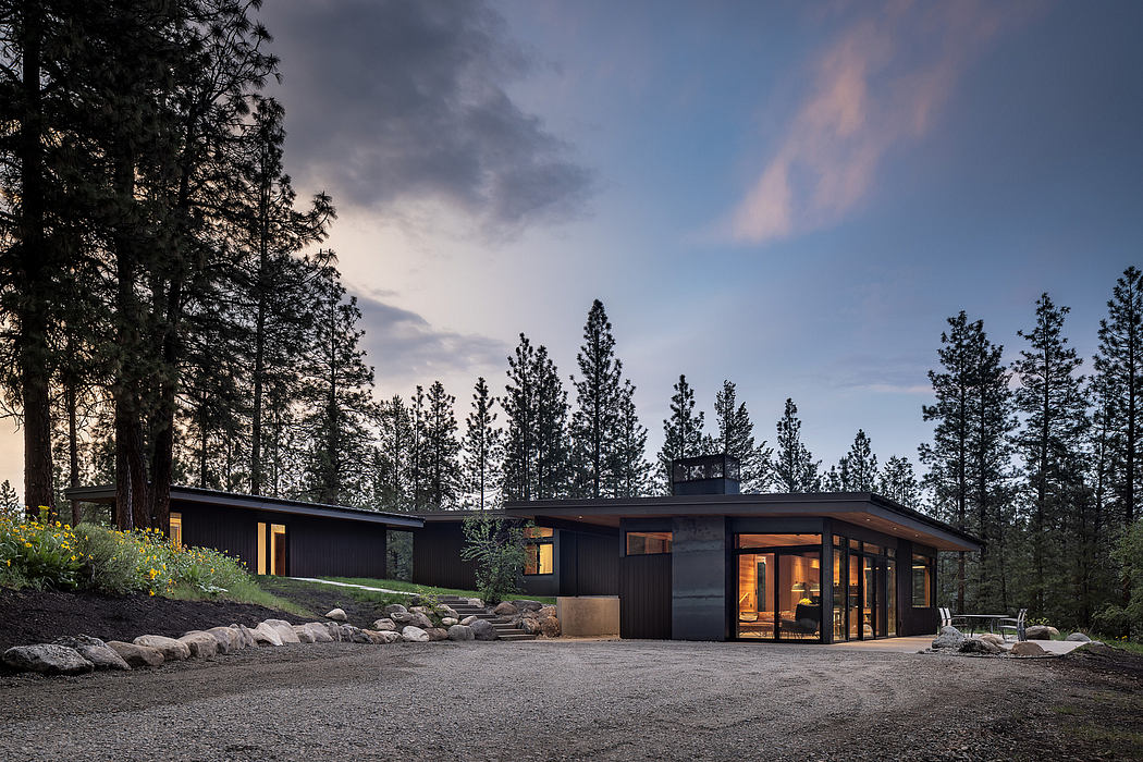 Sleek single-story house with large windows nestled among tall pine trees at dusk