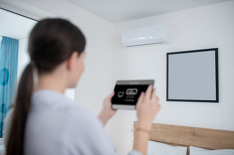 Minimalistic room with a blank screen and a person controlling smart home features on a tablet.