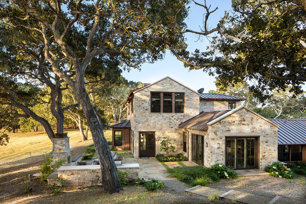Rustic stone façade, expansive windows, and a covered entryway nestled among towering trees.