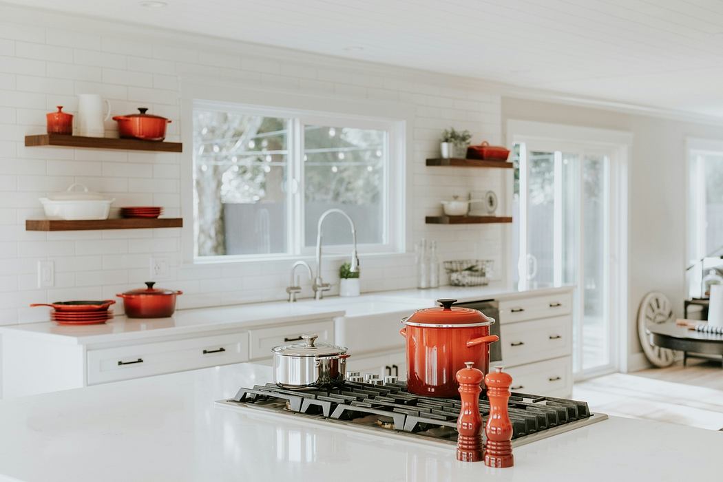 A bright, white kitchen with red cookware and floating shelves.