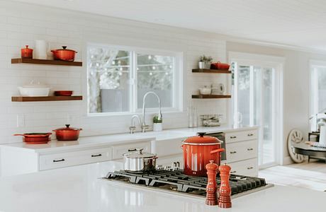 A bright, white kitchen with red cookware and floating shelves.