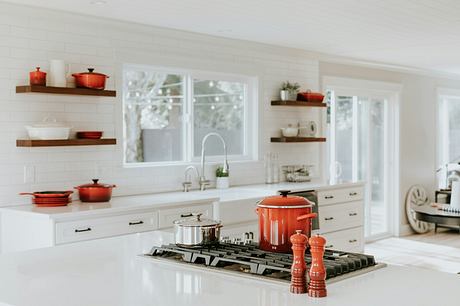 A bright, white kitchen with red cookware and floating shelves.