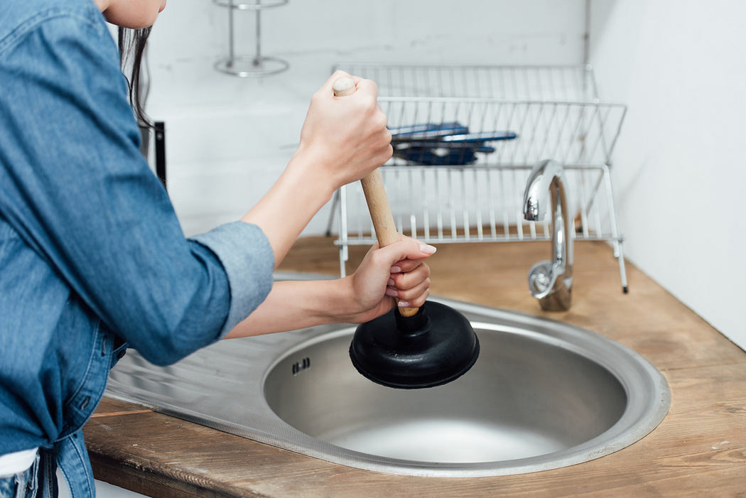 Person using a plunger on a kitchen sink.